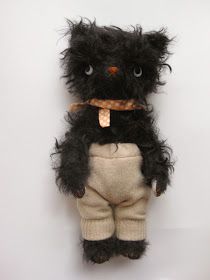 a black stuffed animal with a scarf around it's neck sitting on top of a white wall