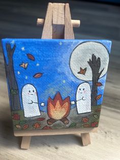 an easel with a painting on it that has two ghost sitting around a campfire