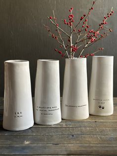 three white vases sitting on top of a wooden table next to a branch with red berries