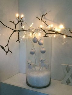 a glass jar filled with snow and christmas ornaments sitting on top of a shelf next to a twig branch