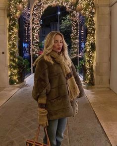 the blonde woman is walking down the street carrying her purse and wearing a fur coat