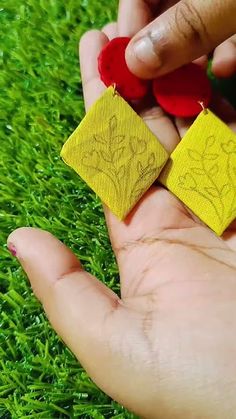 a person is holding two small yellow and red earrings in their hand on the grass