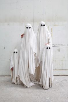 three white ghost statues standing next to each other with black eyes on their faces and arms