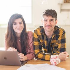 two people sitting at a table with an apple laptop