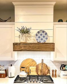 a kitchen with white cabinets and wooden cutting boards on the stove top, surrounded by other utensils