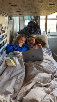 two women laying in bed with an apple laptop