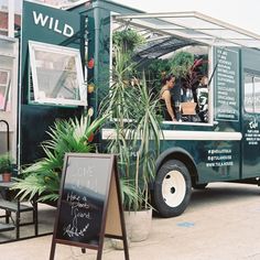 a green food truck parked in front of a building next to a sign with writing on it