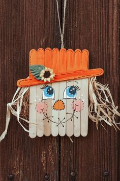 a scarecrow door hanger hanging on a wooden fence with blue eyes and an orange hat