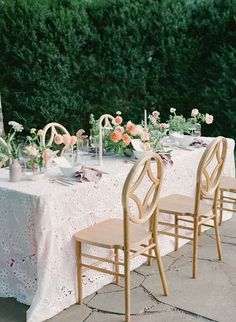 the table is set with pink and white flowers on it, along with two wooden chairs