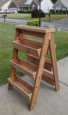 a wooden shelf sitting on the sidewalk in front of a house with grass and houses behind it