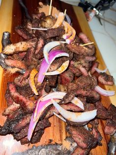 a wooden cutting board topped with meat and onions on skewers next to a knife