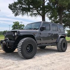 a black jeep parked in front of a tree on top of a dirt road next to a field