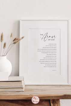 a white vase sitting on top of a wooden table next to a framed print with the words across it