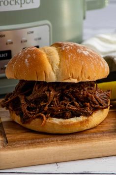 a pulled pork sandwich on a wooden cutting board next to an instant pot roaster