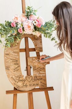 a woman standing next to a easel with flowers on it and writing in the letters