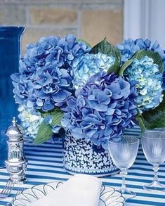 there is a vase with blue flowers in it and two glasses on the table next to it