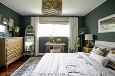 a bedroom with dark green walls and white linens on the bed, along with an antique dresser