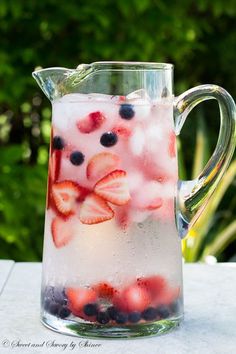 a pitcher filled with ice and berries on top of a table next to plants in the background