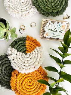 three crocheted coasters on a table next to plants and ring holders with the words made it written across them