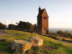 an old church on top of a hill with rocks in the foreground and trees around it