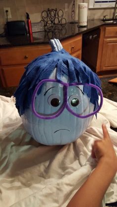 a blue pumpkin with glasses on it's head and a person pointing at it