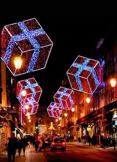 people walking down the street at night with christmas lights and decorations on buildings in the background