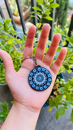 a hand is holding a blue and white keychain in front of some plants