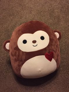 a stuffed animal with a heart on it's chest sits on the floor in front of a carpet