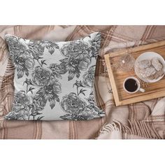 a pillow with flowers on it sitting next to a cup of coffee and a tray