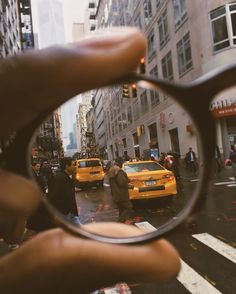 a person holding up a magnifying glass to look at taxi cabs on the street