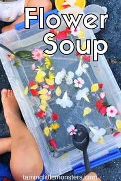 a plastic container filled with flowers sitting on the ground next to a child's feet