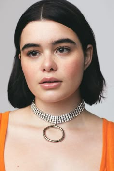 a woman wearing an orange top with a choker on her neck and necklace in the shape of a circle