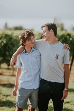 two young men standing next to each other in the middle of a field with trees