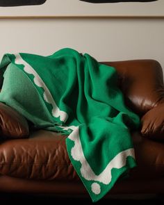 a green and white blanket sitting on top of a brown leather couch next to a painting