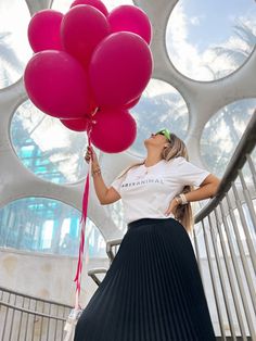 a woman in a white shirt and black pleated skirt holding pink balloons while standing on stairs