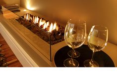 two wine glasses sitting next to each other on a table with a fireplace in the background