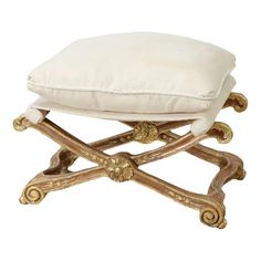 a white cushion sitting on top of a wooden foot stool with gold trimmings