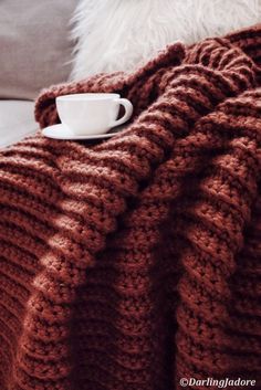 a coffee cup is sitting on the edge of a blanket that's draped over a couch