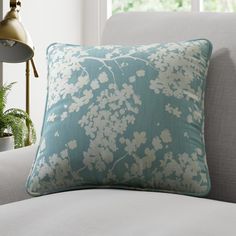 a blue and white pillow sitting on top of a couch next to a plant in a vase