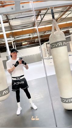 a man taking a selfie in front of two boxing punching bags with his phone