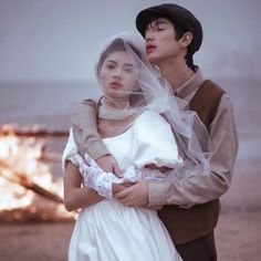 a man and woman standing next to each other in front of a campfire on the beach