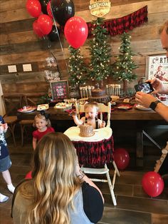 a group of people sitting around a table with cake on it and balloons in the air