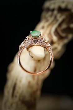 an engagement ring with a green stone in the center on top of a piece of wood