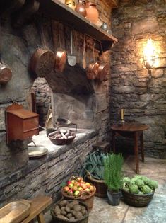 an old stone kitchen with pots and pans hanging from the wall, along with various fruits and vegetables