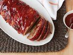 sliced meatloaf on a white plate next to a bowl of ketchup