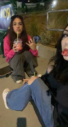 two women sitting on the ground with drinks in their hands and one holding a straw