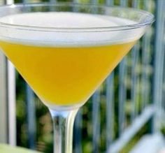 a glass filled with yellow liquid sitting on top of a table next to a railing