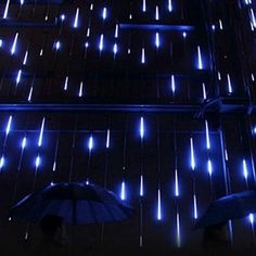 two people with umbrellas standing in front of a wall covered in blue led lights