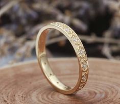 a gold wedding ring with small diamonds on top of a piece of tree stump in front of some dried flowers