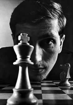 black and white photograph of a young man with his head on a chess board looking at the queen